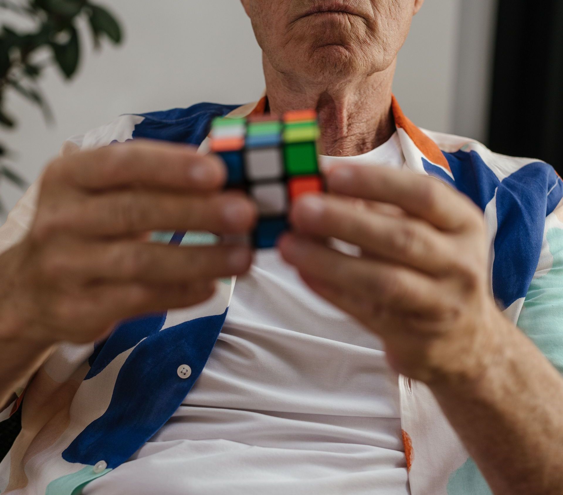 Elderly man focusing on solving a Rubik's Cube indoors, demonstrating concentration and puzzle-solving skills.